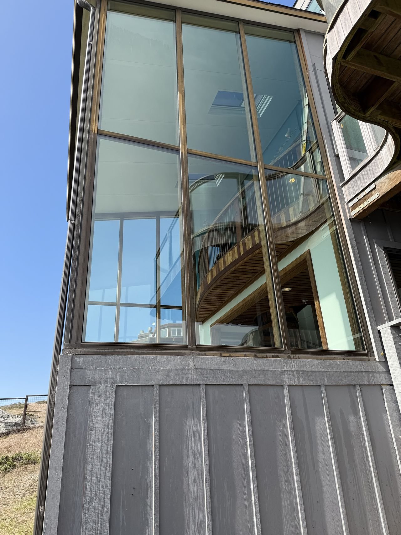 A two-story wall of glass showing a curved wooden balcony inside