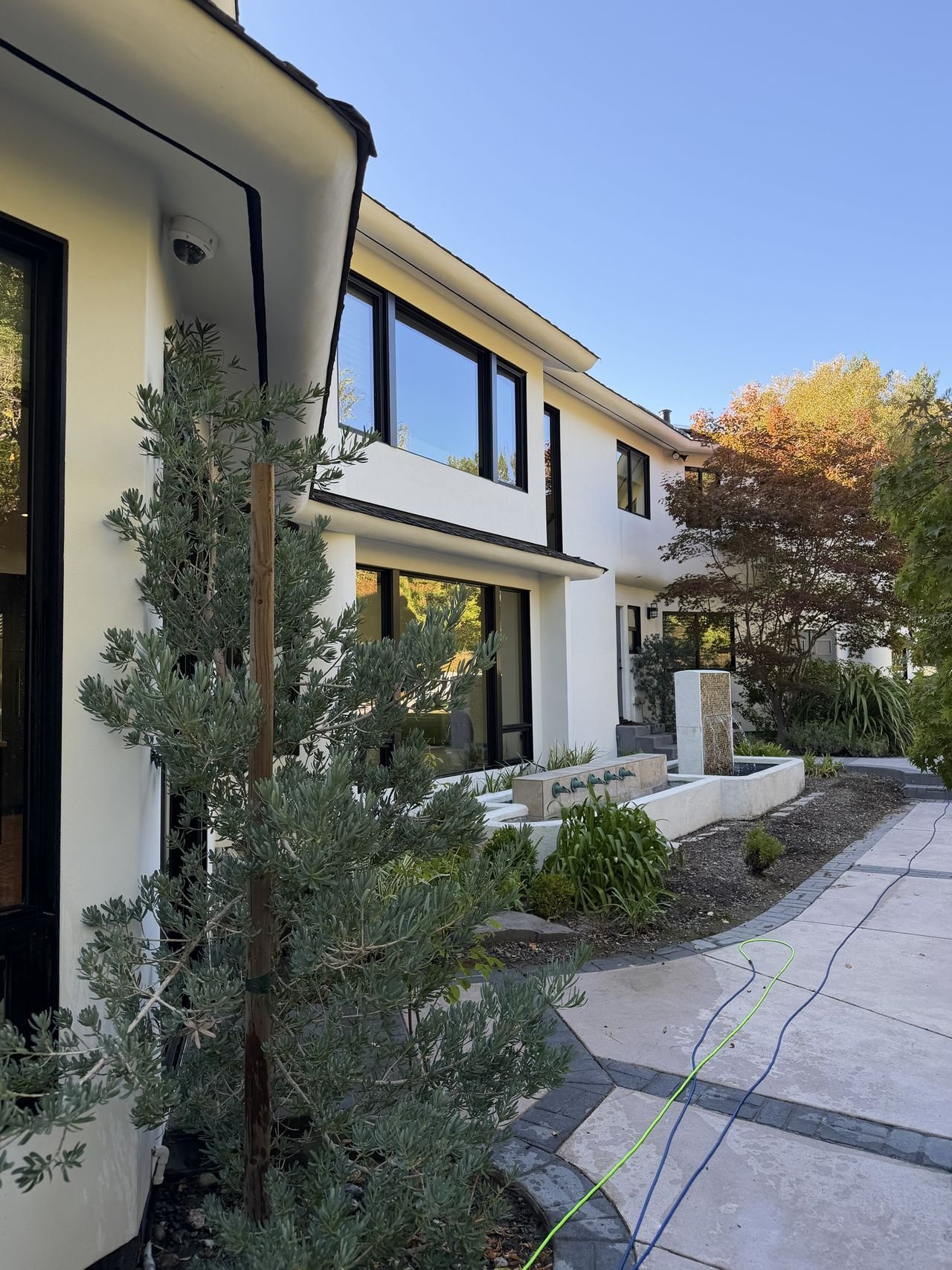 A white home with large black-framed windows above a courtyard fountain and autumn trees