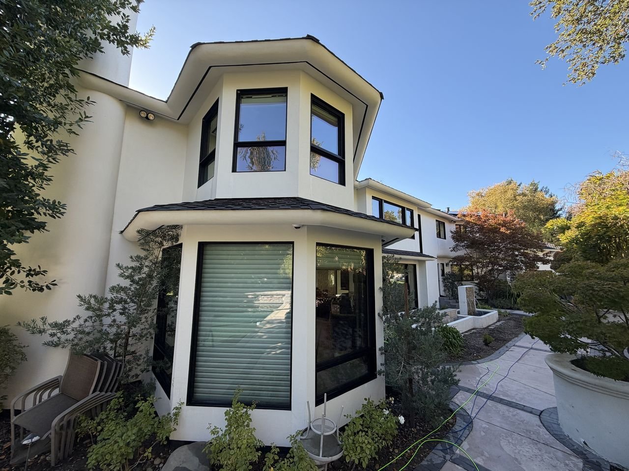 A white two-story octagonal bay with large black-framed windows beside a garden path