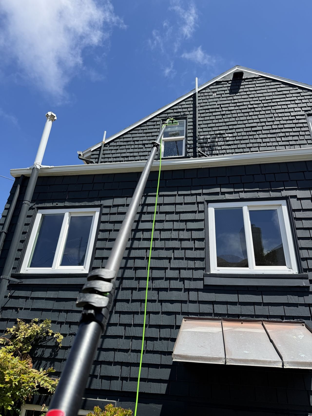 A water-fed pole rinsing an attic window high on a dark shingled house