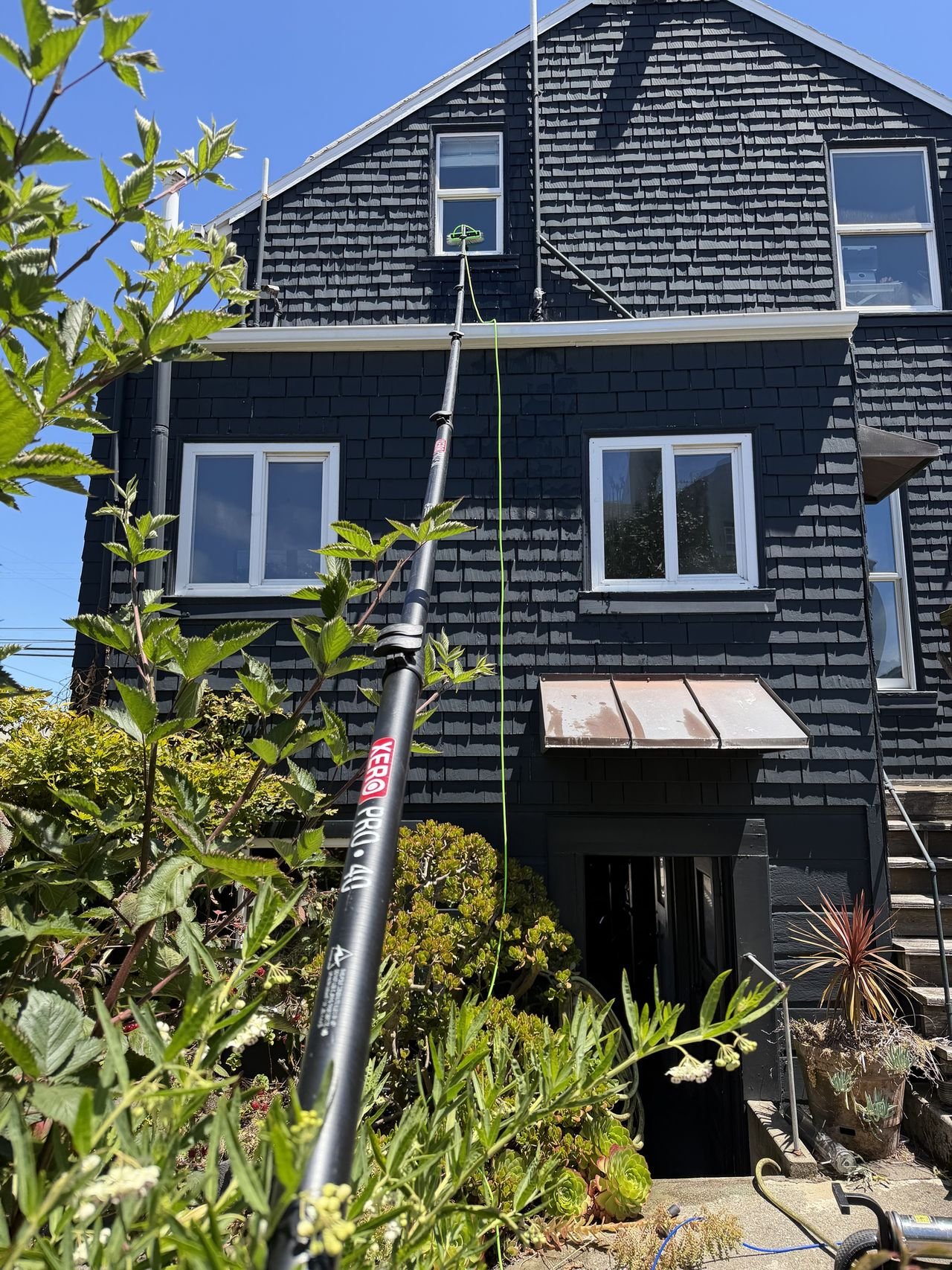 A water-fed pole reaching an attic window above the gutter of a dark shingled house