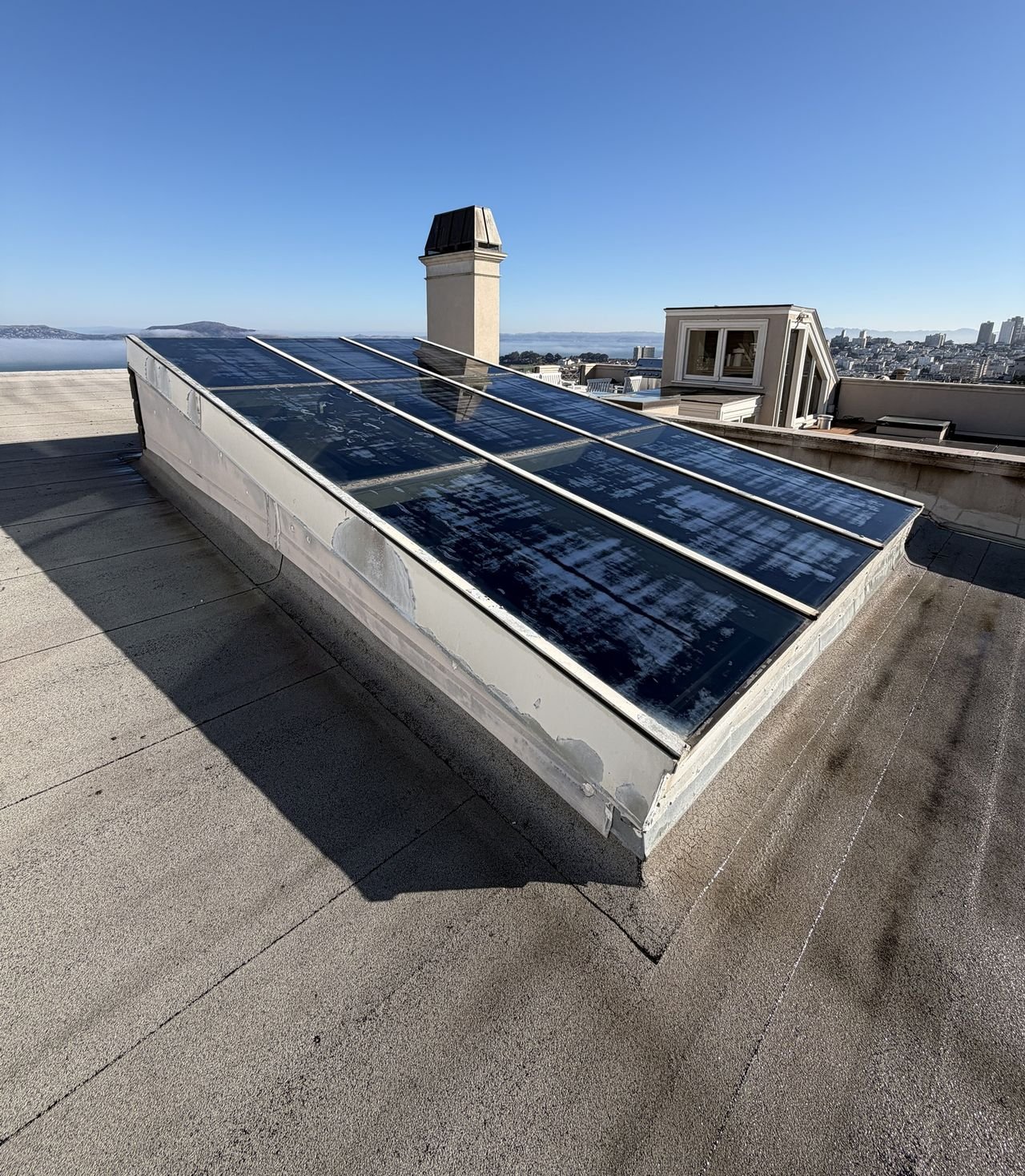 Before cleaning: a large rooftop skylight clouded with white mineral buildup, with the bay, fog and hills behind