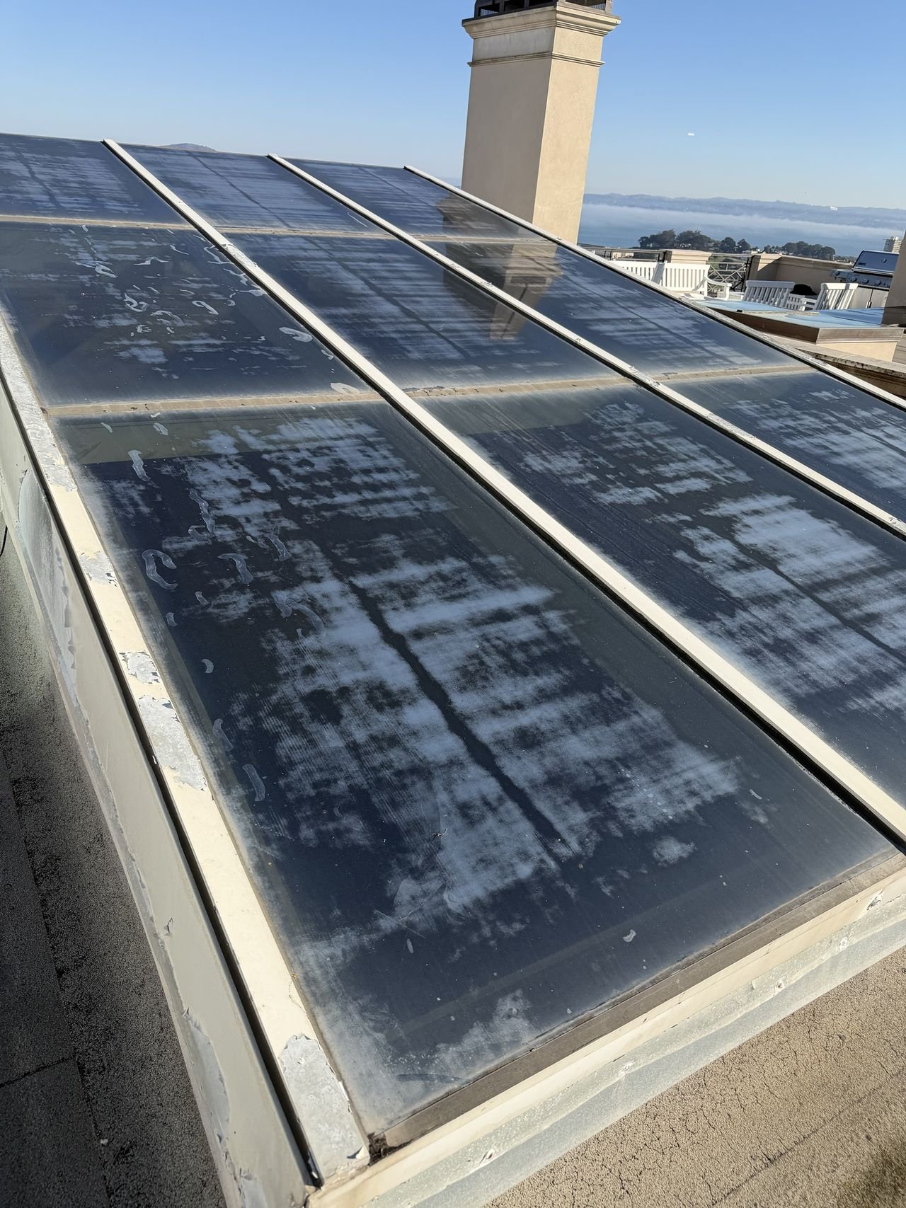 Close-up before cleaning: thick white mineral deposits across a skylight, with the bay in the distance