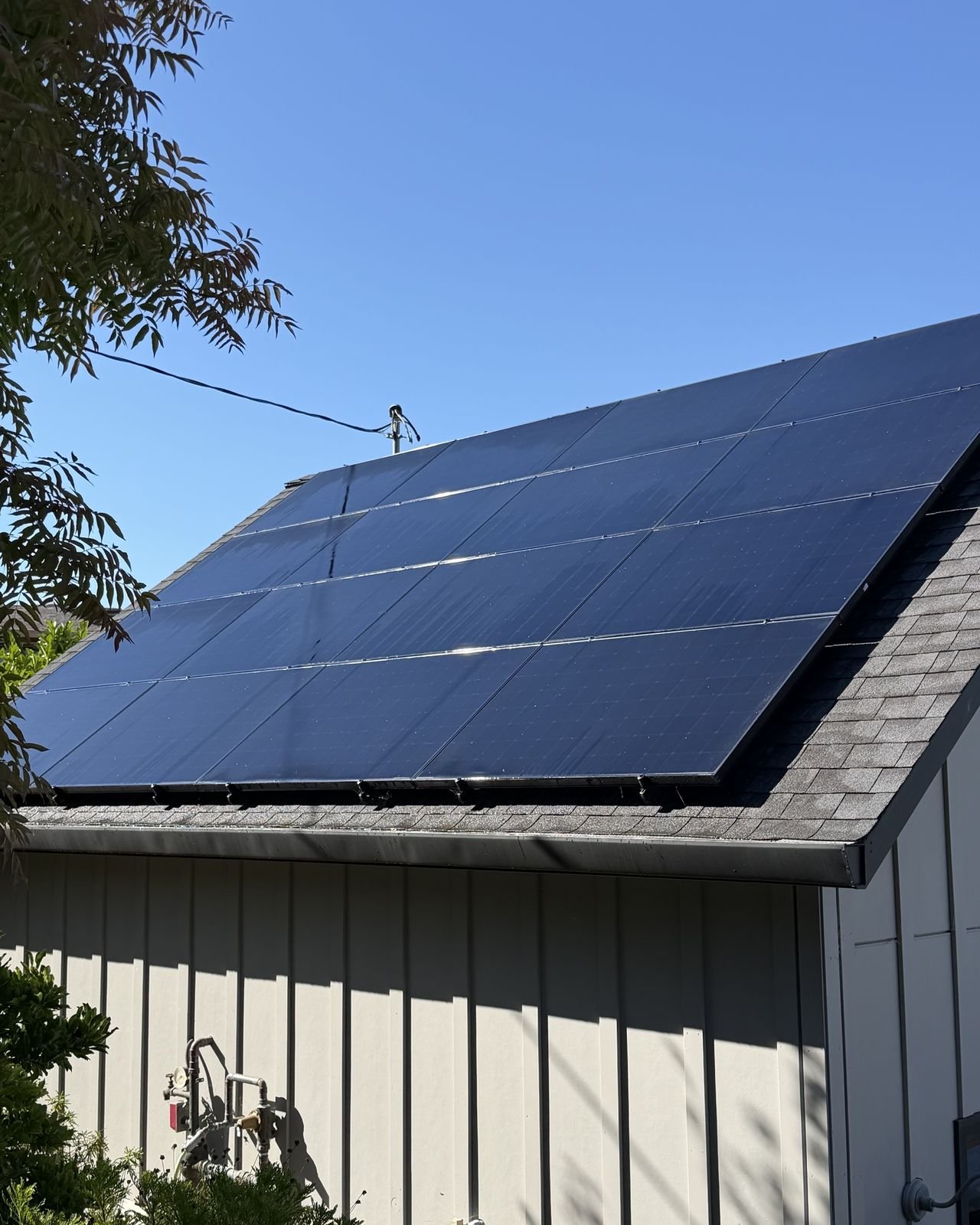 A full array of cleaned black solar panels on a gabled roof under a blue sky