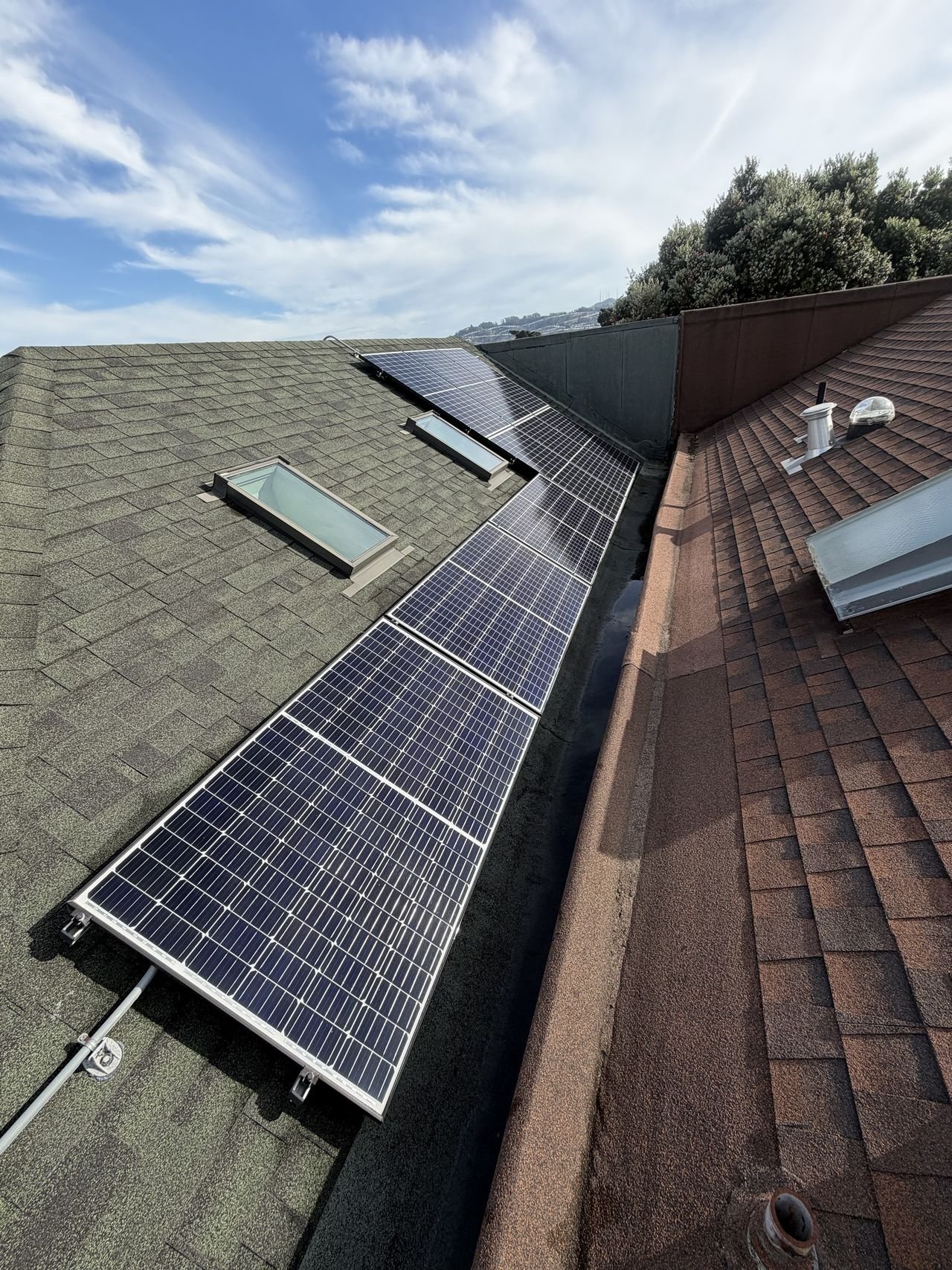 A long row of cleaned solar panels wrapping around two skylights under a cloudy blue sky