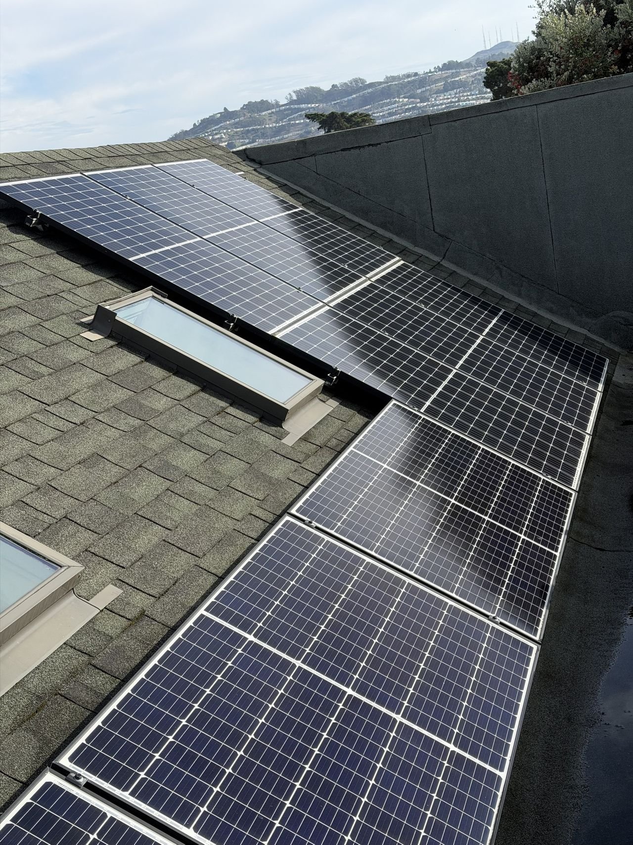 Rows of cleaned solar panels and skylights on a roof, with San Francisco's hills and Sutro Tower behind