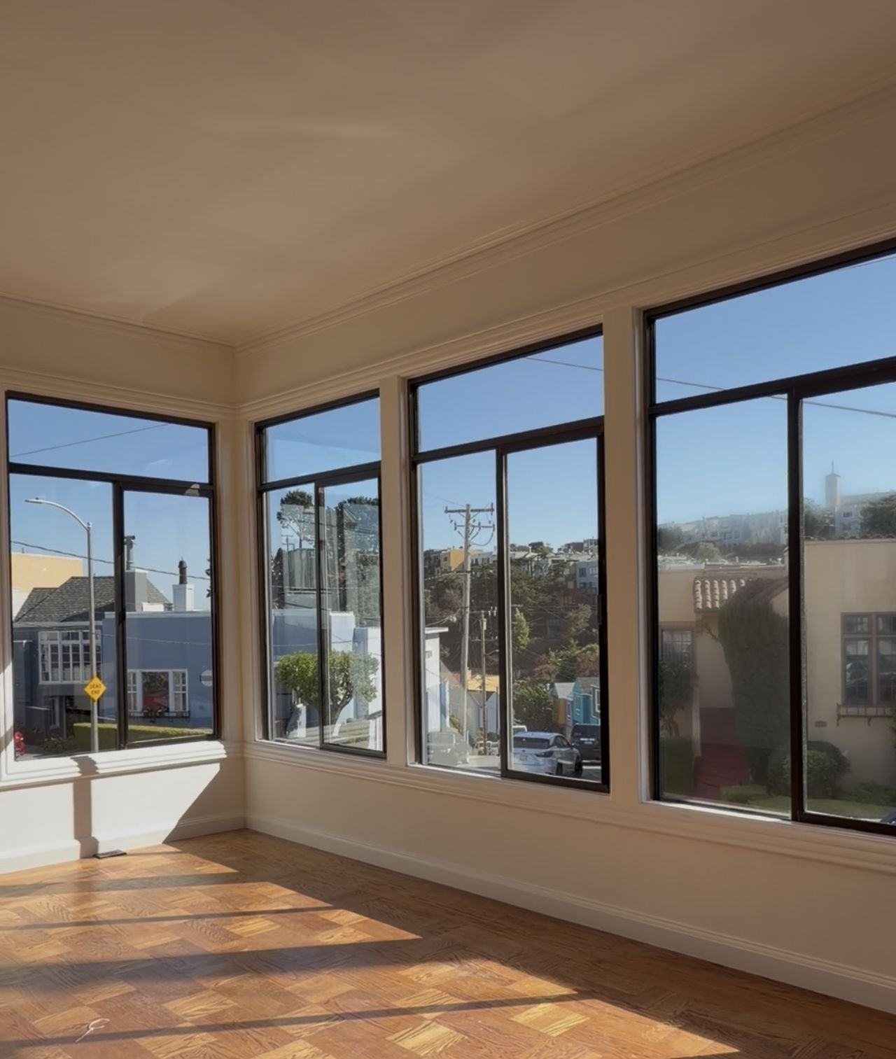 A sunny, empty room with a corner of tall, freshly cleaned windows and sunlight across a parquet floor