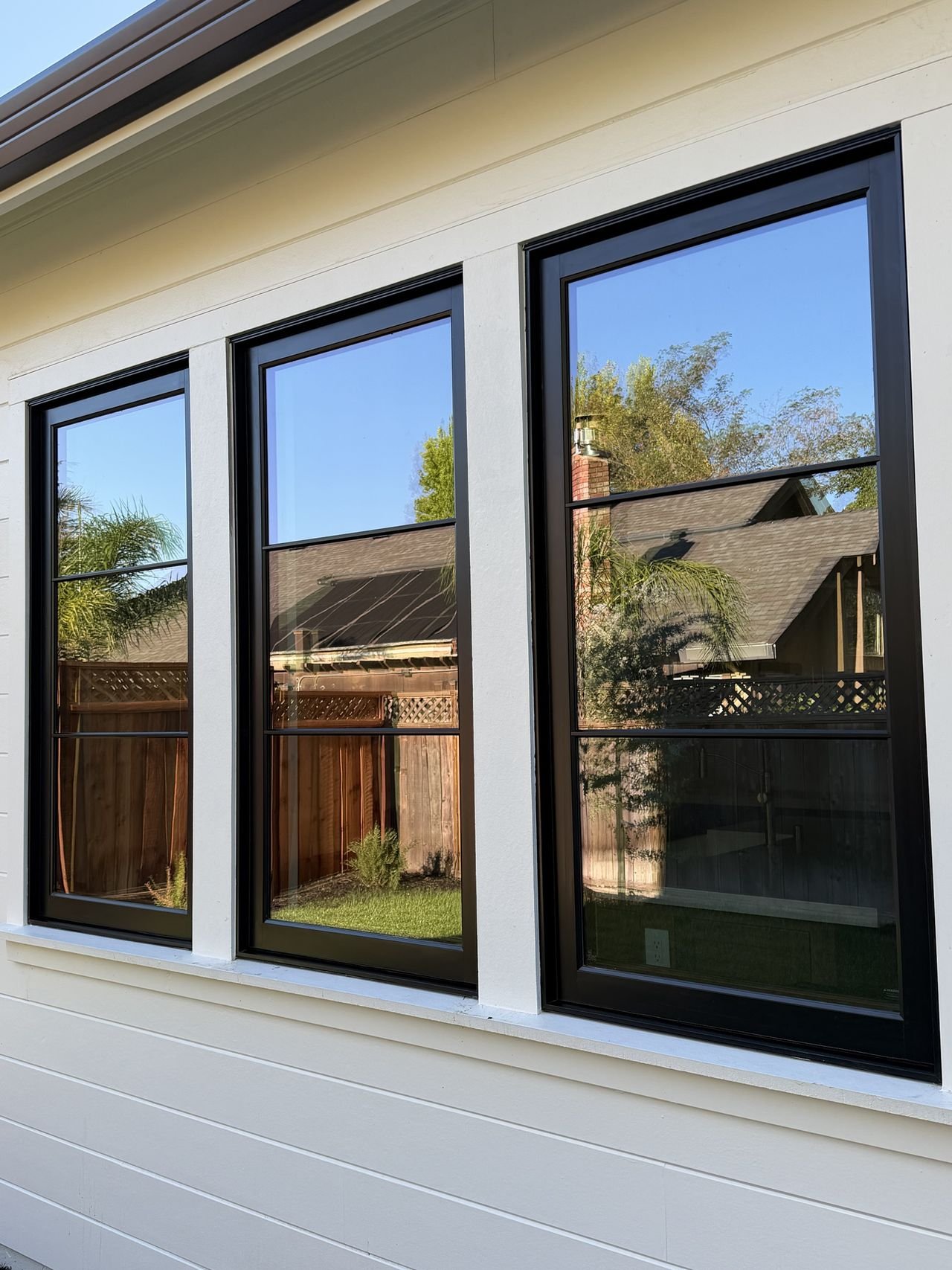 Three black-framed windows so clean they mirror the trees, fence and sky