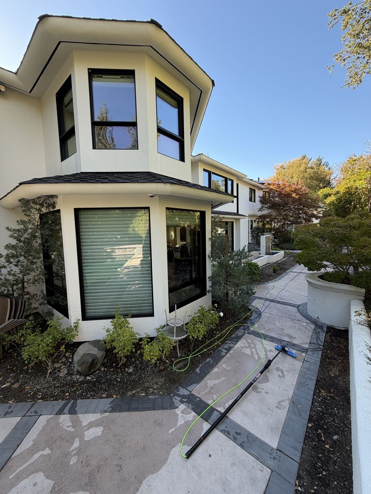 A water-fed pole and hoses on a garden path beside a two-story home